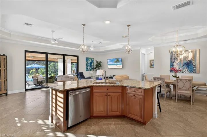 Kitchen featuring a raised ceiling, suspended lighting, crown molding, an island with sink, and wood finish cabinets