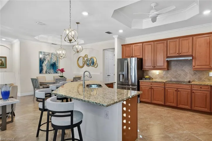 Kitchen featuring ornamental molding, wood finish cabinetry, ceiling fan, a raised ceiling, and light stone countertops
