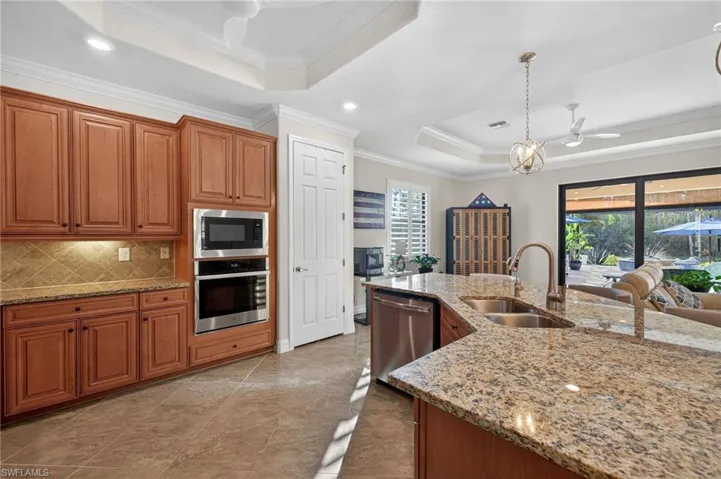 Kitchen with a ceiling fan, a raised ceiling, stainless steel appliances, wood finish cabinets, and light stone countertops
