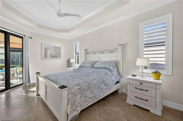 Bedroom with access to exterior, a raised ceiling, a ceiling fan, crown molding, and dark tile patterned floors