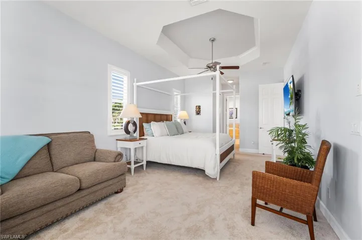Oversized primary bedroom with a tray ceiling, light carpet, and ceiling fan.