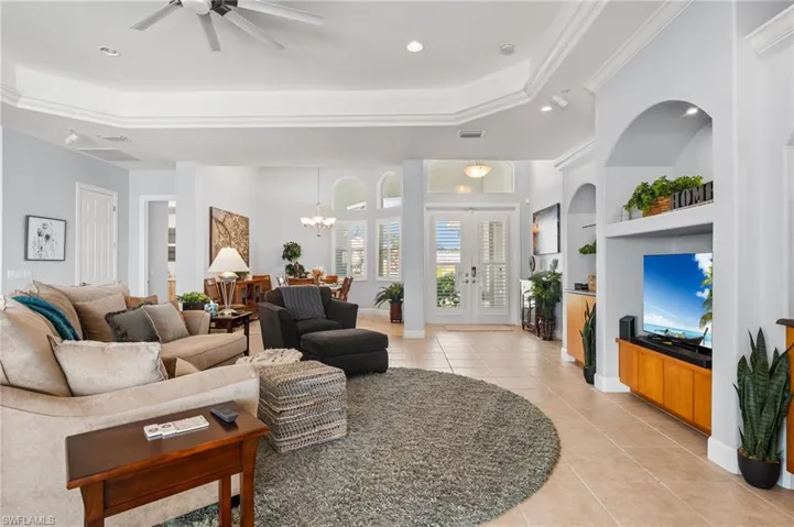 Living room featuring crown molding, a tray ceiling, light tile patterned floors, and ceiling fan.