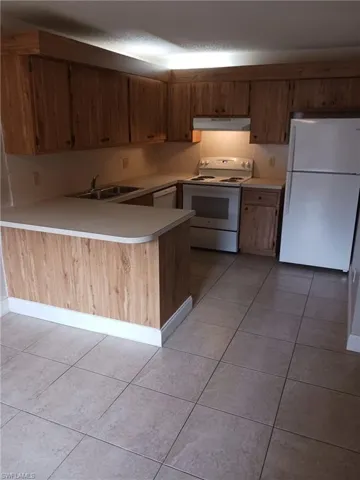Kitchen with white appliances, light tile patterned floors, light countertops, a peninsula, and a textured ceiling