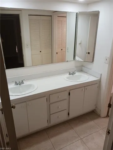 Full bath with a closet, double vanity, and light tile patterned flooring