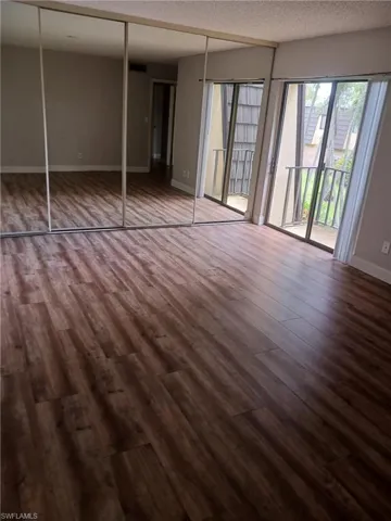 Unfurnished bedroom featuring wood finished floors, access to outside, a textured ceiling, and a closet