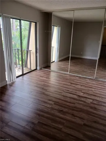 Unfurnished bedroom featuring dark wood-style flooring, a textured ceiling, access to exterior, and a closet