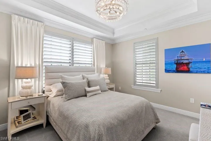 Carpeted bedroom with a chandelier, multiple windows, crown molding, and a raised ceiling