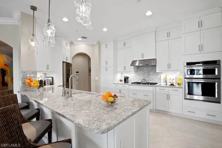 Kitchen with arched walkways, a peninsula, a breakfast bar area, white cabinetry, and light stone counters