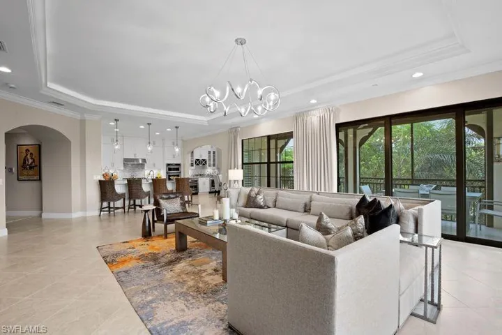 Living area with arched walkways, a tray ceiling, crown molding, and a chandelier