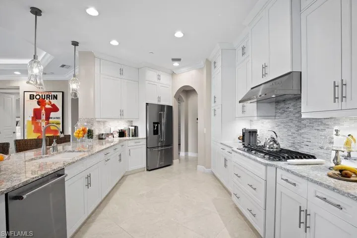 Kitchen featuring crown molding, arched walkways, stainless steel appliances, and white cabinetry