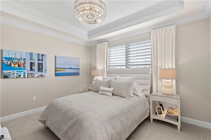 Bedroom with ornamental molding, hanging lights, light colored carpet, and a raised ceiling