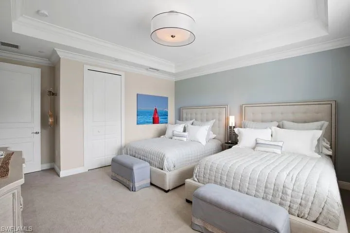 Bedroom with a tray ceiling, light carpet, crown molding, and a closet