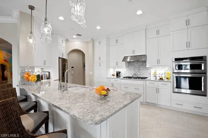 Kitchen with arched walkways, a breakfast bar area, a peninsula, white cabinets, and light stone countertops