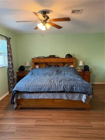 Bedroom with a textured ceiling, wood finished floors, and a ceiling fan