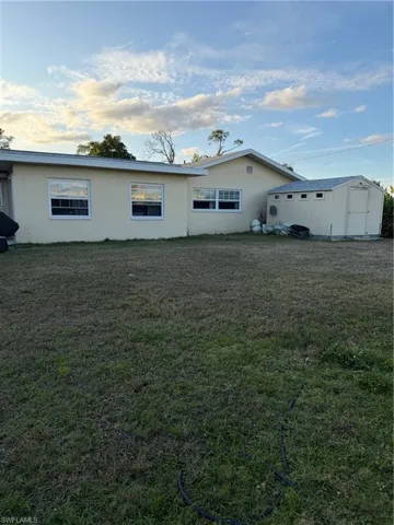 Rear view of house with a storage unit, stucco siding, and a lawn
