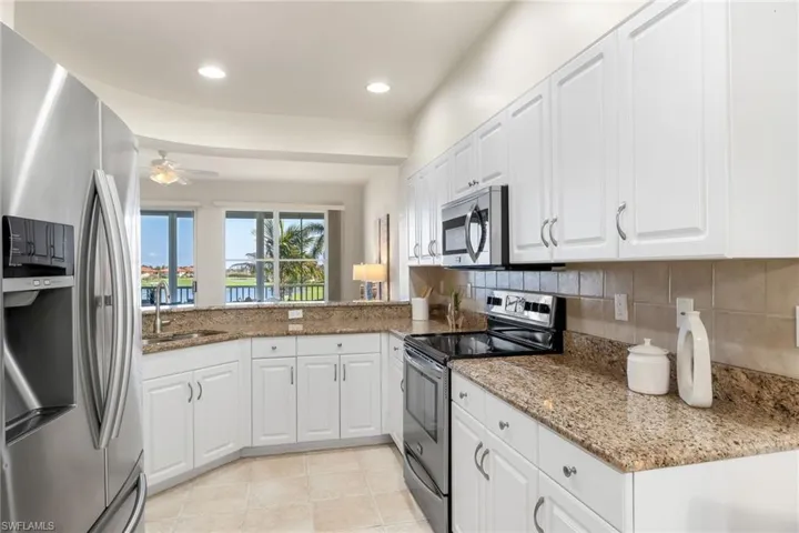 Kitchen featuring stainless steel appliances, modern white cabinetry, stylish backsplash, light stone granite countertops, and tile floors.