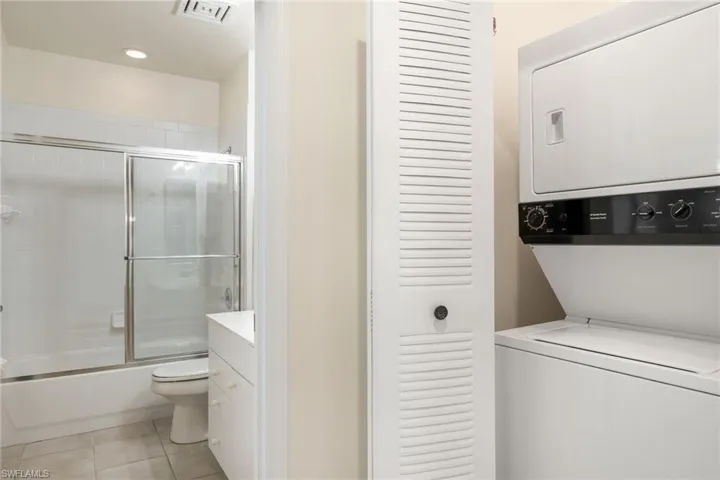 Clothes washing area featuring stacked washing maching and dryer and light tile patterned floors
