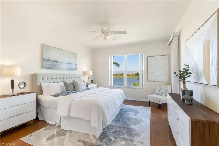 Oversized Primary Bedroom featuring a breathtaking water view, siting area, door to screened lanai. wood floors, walk in closet, and a ceiling fan