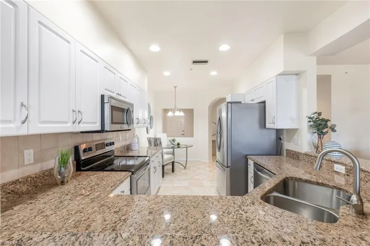 Kitchen featuring stainless steel appliances, modern white cabinetry, stylish backsplash, light stone granite countertops, and tile floors