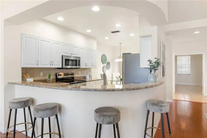 Kitchen with tasteful backsplash, appliances with stainless steel finishes, granite countertops, and breakfast bar/eating area with stools