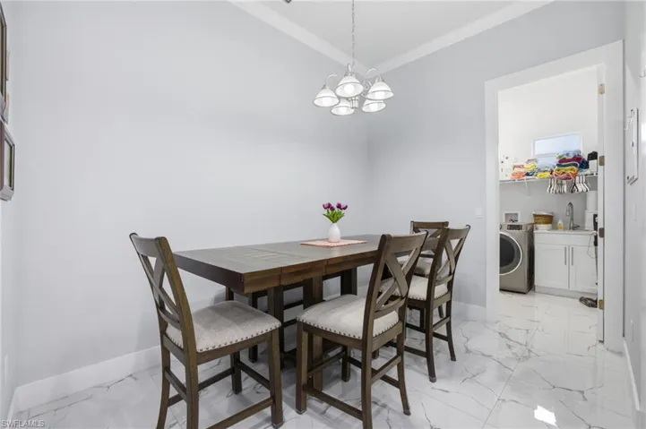 Dining room with light marble finish floors, washer / dryer, a chandelier, and crown molding