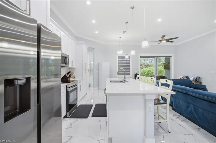 Kitchen featuring appliances with stainless steel finishes, open floor plan, white cabinets, crown molding, and light marble finish flooring