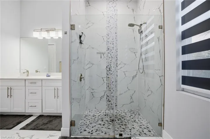 Full bath featuring a marble finish shower, double vanity, and dark marble finish floors