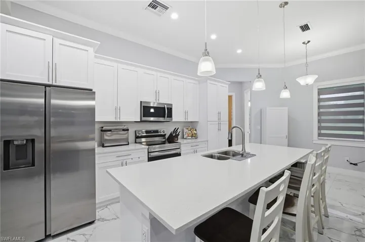 Kitchen featuring appliances with stainless steel finishes, light marble finish flooring, ornamental molding, white cabinetry, and light stone countertops