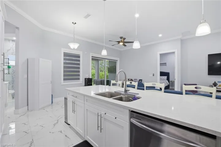 Kitchen featuring stainless steel dishwasher, white cabinets, light stone countertops, ornamental molding, and decorative light fixtures