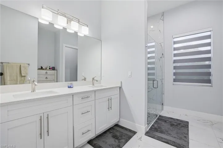 Full bathroom featuring double vanity, light marble finish flooring, and a marble finish shower