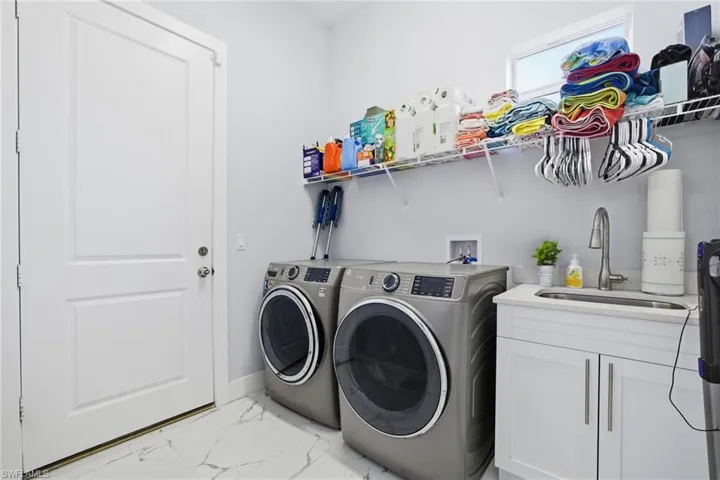 Washroom featuring light marble finish floors, washing machine and clothes dryer, and cabinet space