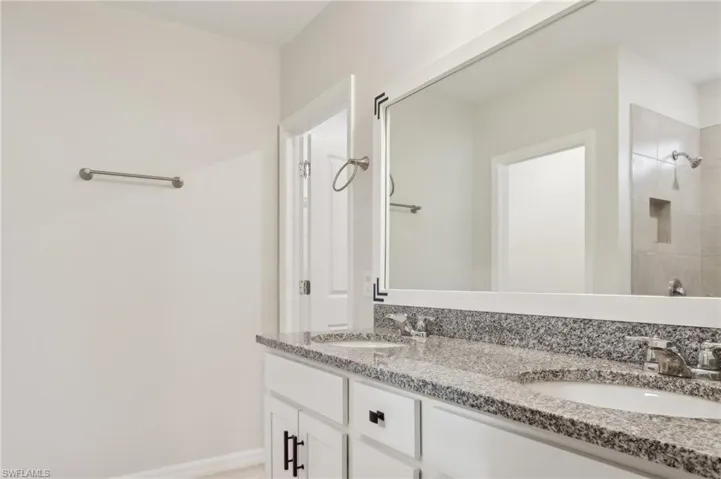 Full bathroom featuring baseboards, double vanity, a sink, and a tile shower