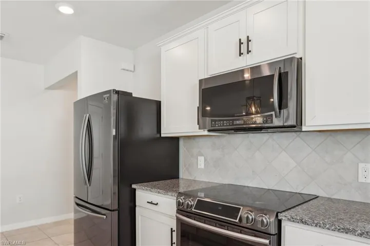Kitchen featuring white cabinets, light tile patterned floors, stainless steel appliances, and backsplash