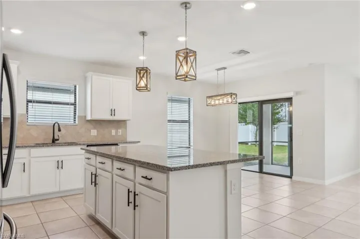 Kitchen with tasteful backsplash, a center island, light tile patterned flooring, a sink, and visible vents
