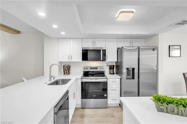 Kitchen with stainless steel appliances, white cabinets, light stone counters, recessed lighting, and light wood finished floors