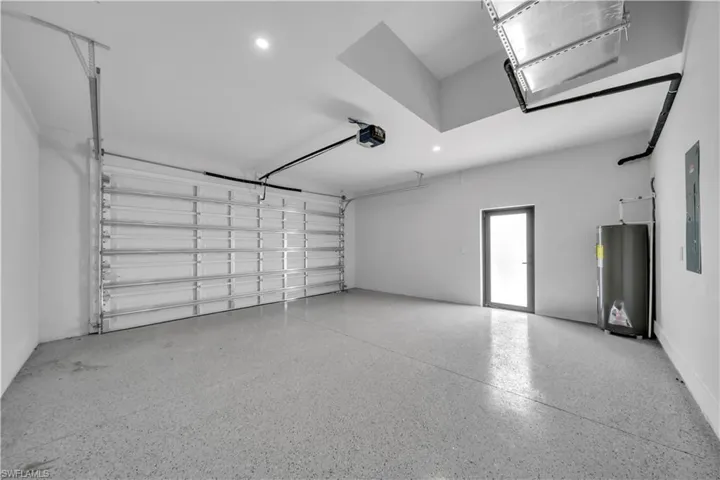 Spacious garage featuring a finished epoxy floor, an overhead garage door with an automatic opener, a frosted glass entry door, a hot water heater, and an electrical panel