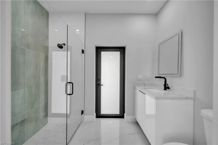 Modern bathroom featuring a frameless glass shower enclosure with matte black hardware, a tiled shower wall, and coordinating marble-look flooring