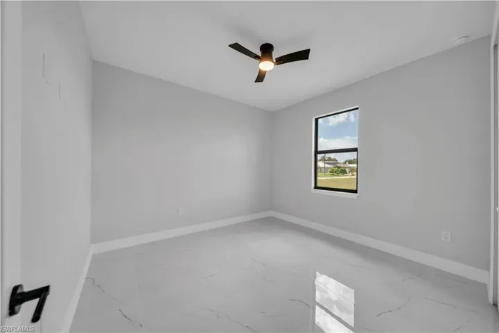 Spacious room featuring large format tile flooring, a window with black trim, a ceiling fan with integrated lighting, clean white baseboards, and neutral wall paint