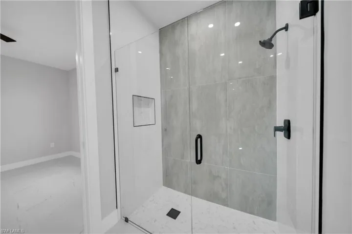Frameless glass shower enclosure featuring large format grey wall tiling, a built-in shower niche, and matte black fixtures