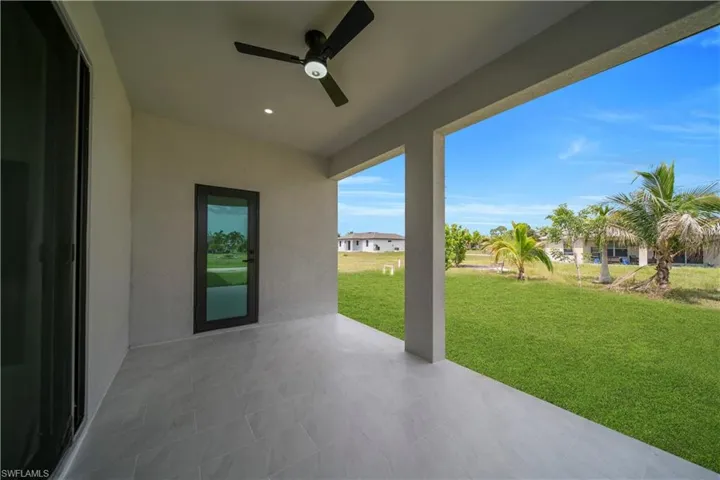 Covered patio featuring large format tile flooring, a ceiling fan, and recessed lighting, opening to a spacious lawn with palm trees