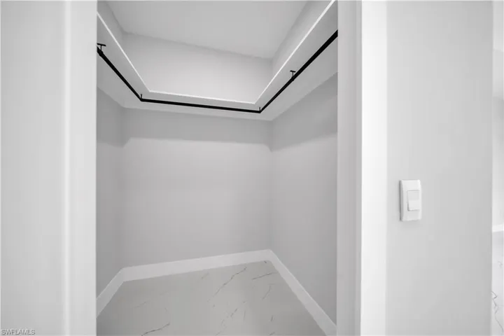 Walk-in closet with perimeter hanging rods, recessed ceiling lighting, light gray walls, and white marble-patterned flooring