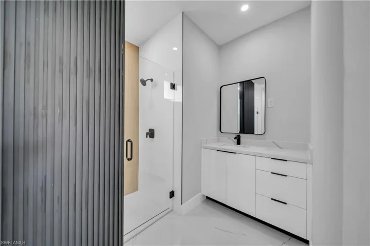 Modern bathroom with a glass-enclosed shower, white vanity with integrated sink, black framed mirror, and recessed lighting