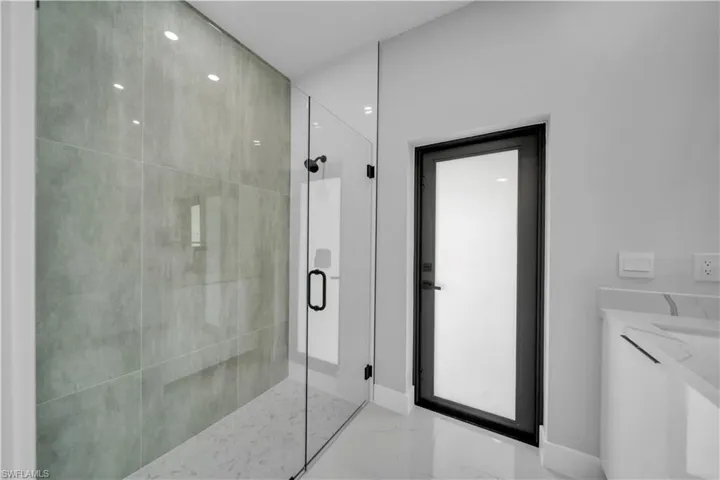 Spacious walk-in shower featuring large format grey tile, glass enclosure, and a built-in bench