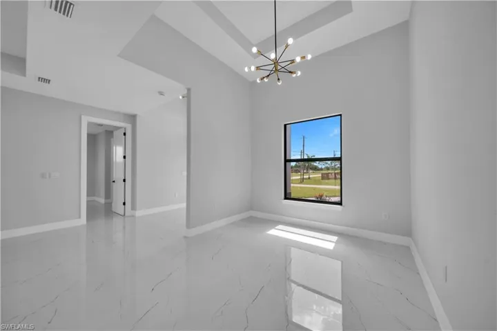 Spacious interior room featuring high ceilings with a tray ceiling detail, a modern sputnik-style chandelier, large black-framed window, and polished tile flooring with subtle veining