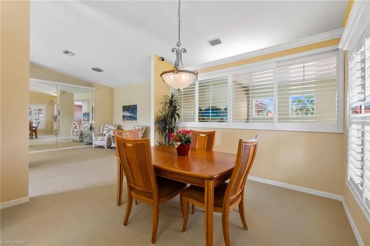 Carpeted dining space featuring a healthy amount of sunlight, baseboards, vaulted ceiling, and visible vents