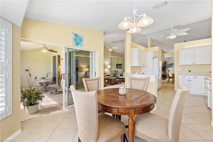 Dining area featuring light tile patterned floors, visible vents, ceiling fan with notable chandelier, and vaulted ceiling