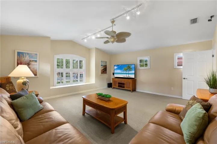 Carpeted living room featuring visible vents, ceiling fan, baseboards, and vaulted ceiling