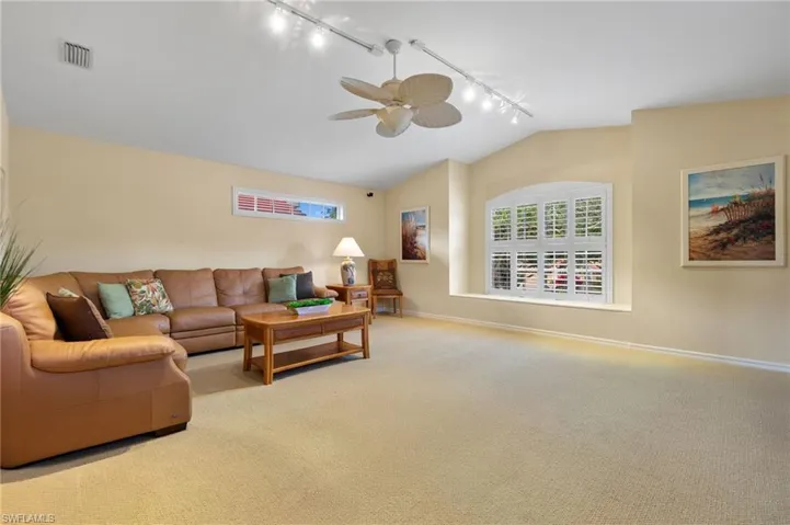 Carpeted living room with ceiling fan, rail lighting, vaulted ceiling, visible vents, and baseboards