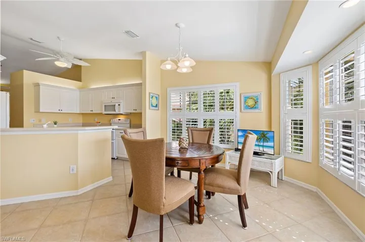 Dining space with ceiling fan with notable chandelier, light tile patterned floors, visible vents, lofted ceiling, and baseboards