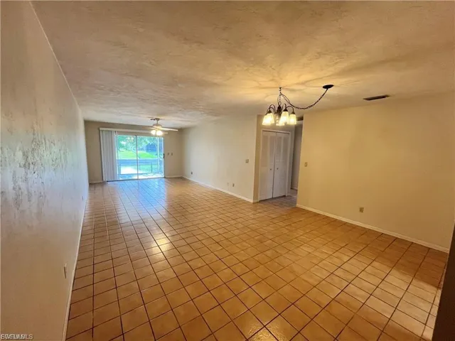Empty room featuring light tile patterned floors, a textured ceiling, a ceiling fan, and a chandelier